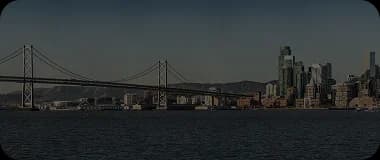 Aerial view of Oakland with the Bay Bridge and city skyline under a cloudy sky.