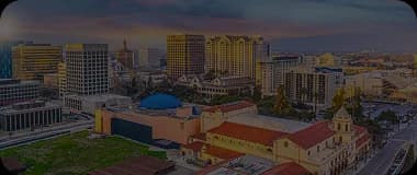Aerial view of San Jose with downtown buildings and surrounding hills under a clear sky.