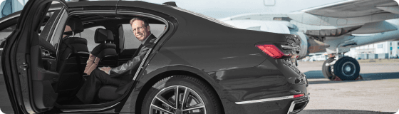 Business traveler steps into luxury sedan on airport tarmac, aircraft in the background for seamless aviation transfers.