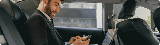 Executive in the backseat uses smartphone and laptop, reflecting productivity-focused rides for fintech professionals.
