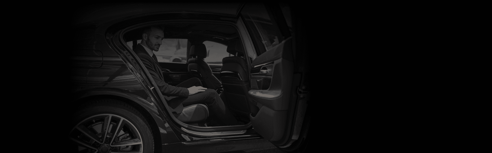 Corporate Event Transportation featuring a sharply dressed man seated in a sleek black luxury sedan, viewed from a wide open-door angle.