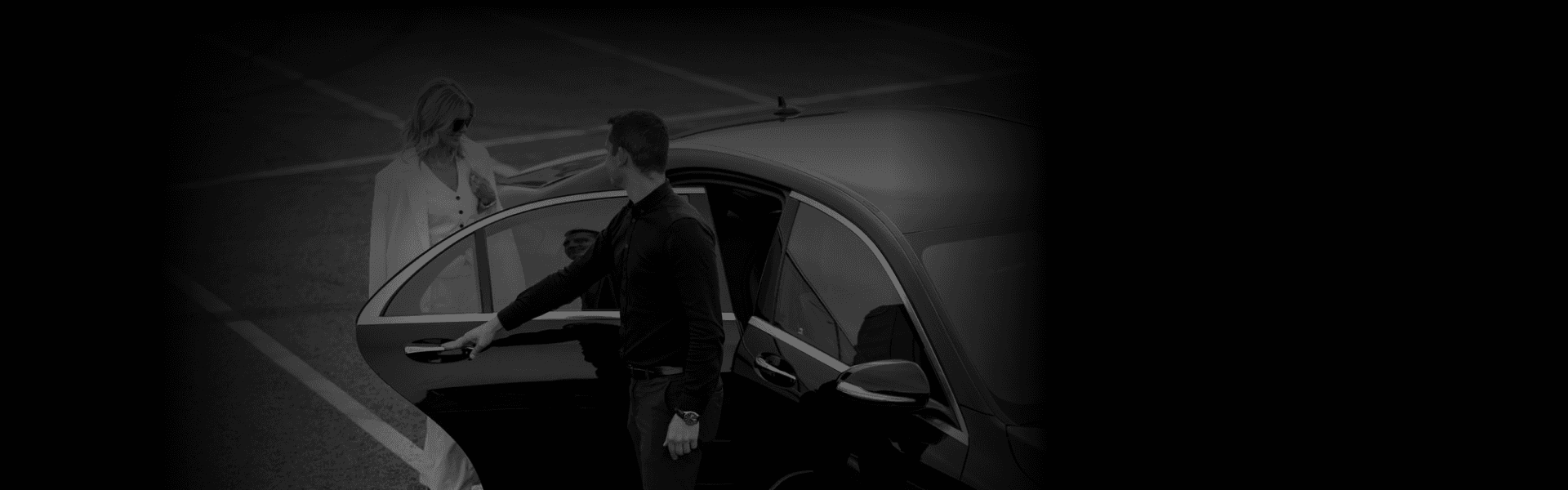 A man opening the rear door of a sleek black sedan for a stylish woman in white, showcasing upscale limo service from a side-angle view.