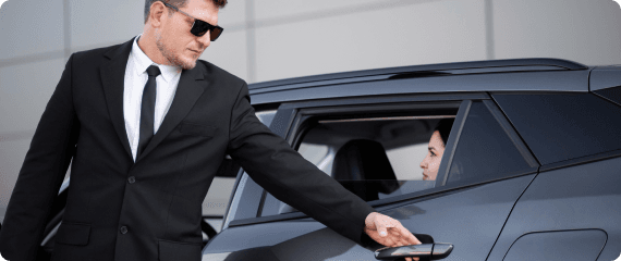 A chauffeur in a black suit opening the car door for a woman, showcasing elite executive arrival service.