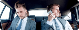 Business professionals in suits are seated in a luxury car, engaged in a focused discussion during a corporate transfer.