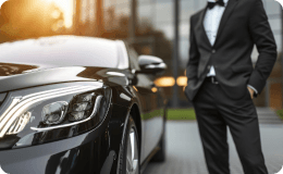 Well-dressed chauffeur in front of a sleek black luxury vehicle, symbolizing refined, professional service.