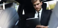 Man in a suit working on a laptop in the backseat of a luxury car.