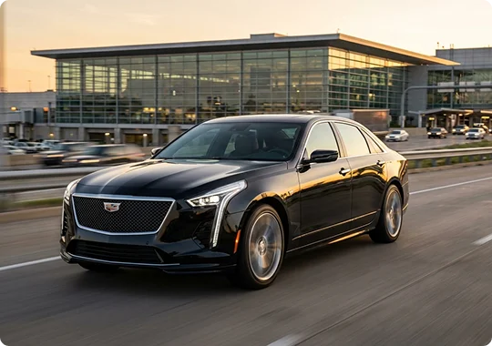 A black Cadillac CT6 in fast motion on a rodaway in front of an airport terminal.