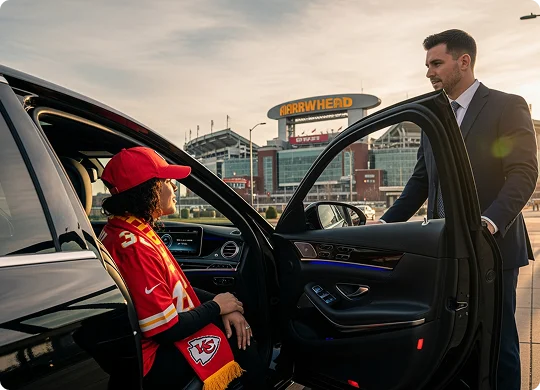 A professional chauffeur in a suit opens the door of a black luxury sedan for a woman dressed in Kansas City Chiefs fan gear, including a red jersey, hat, and scarf. They are parked outside Arrowhead Stadium, which is clearly visible in the background under a warm, late-afternoon sky.