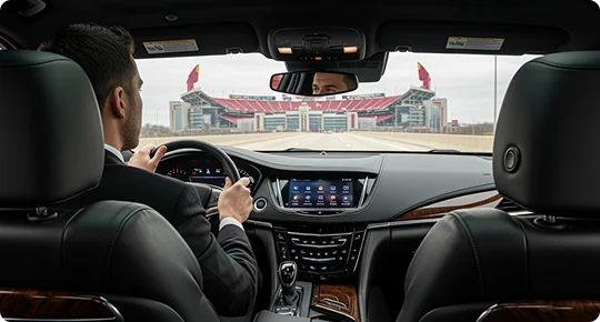 Interior back seat to front view of a luxury car where a chauffeur is driving towards a stadium.