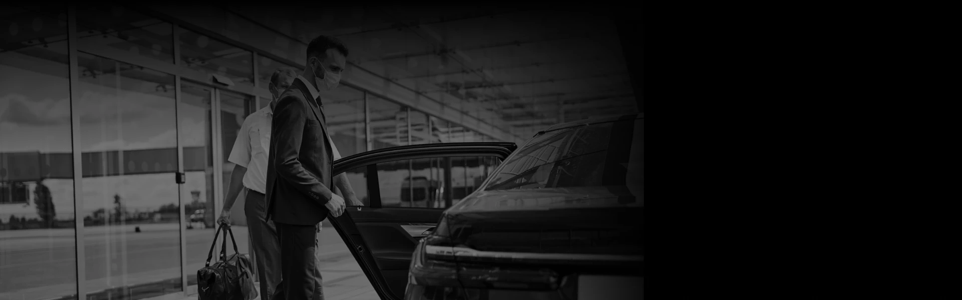 Two men in suits, one masked, load luggage beside a sleek black car at curbside—angled for a seamless airport transfer experience.